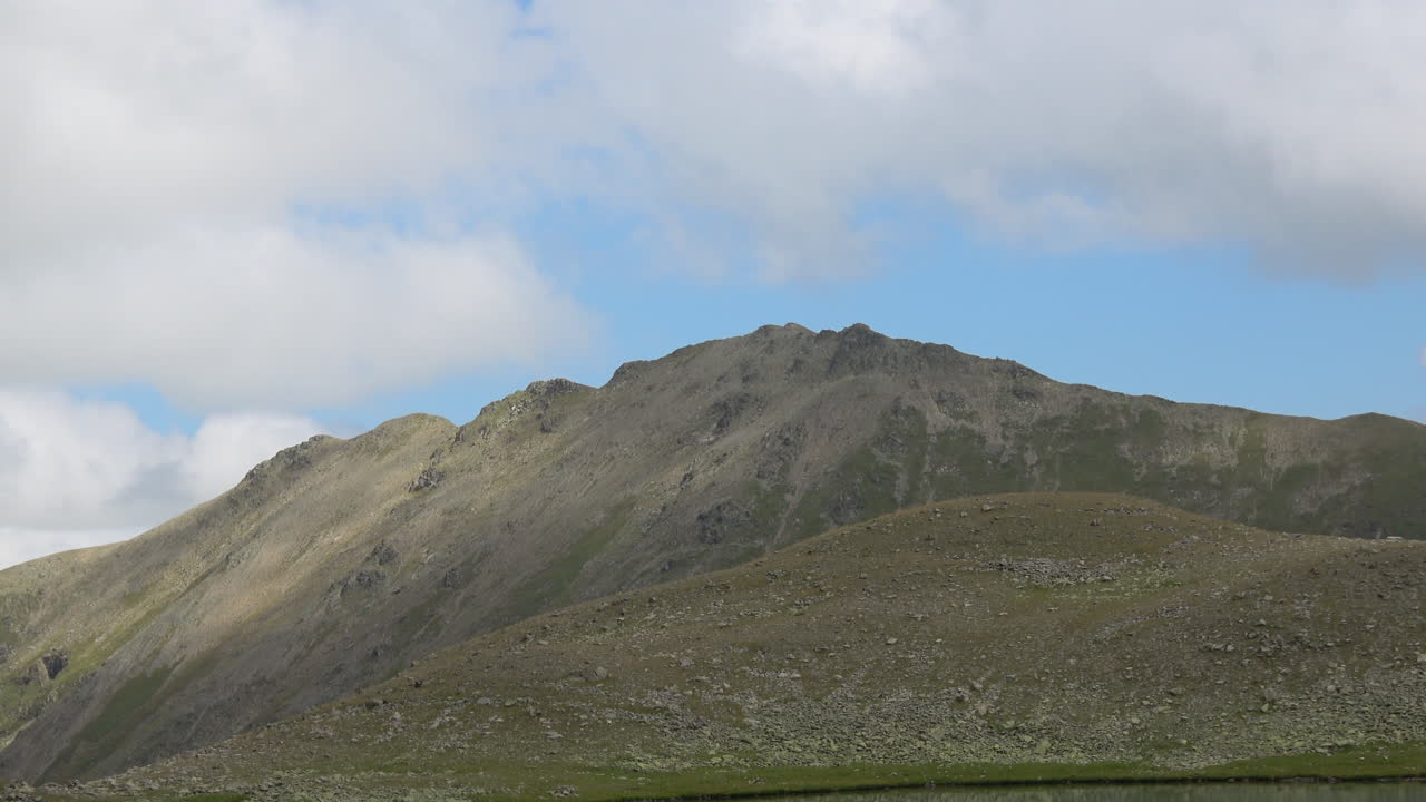 Ampia inquadratura di una cresta montuosa rocciosa e di un verde pendio alpino sotto un cielo azzurro nuvoloso vicino a Dombay, Caucaso, Russia, ideale per temi di viaggio, natura e attività all'aperto.