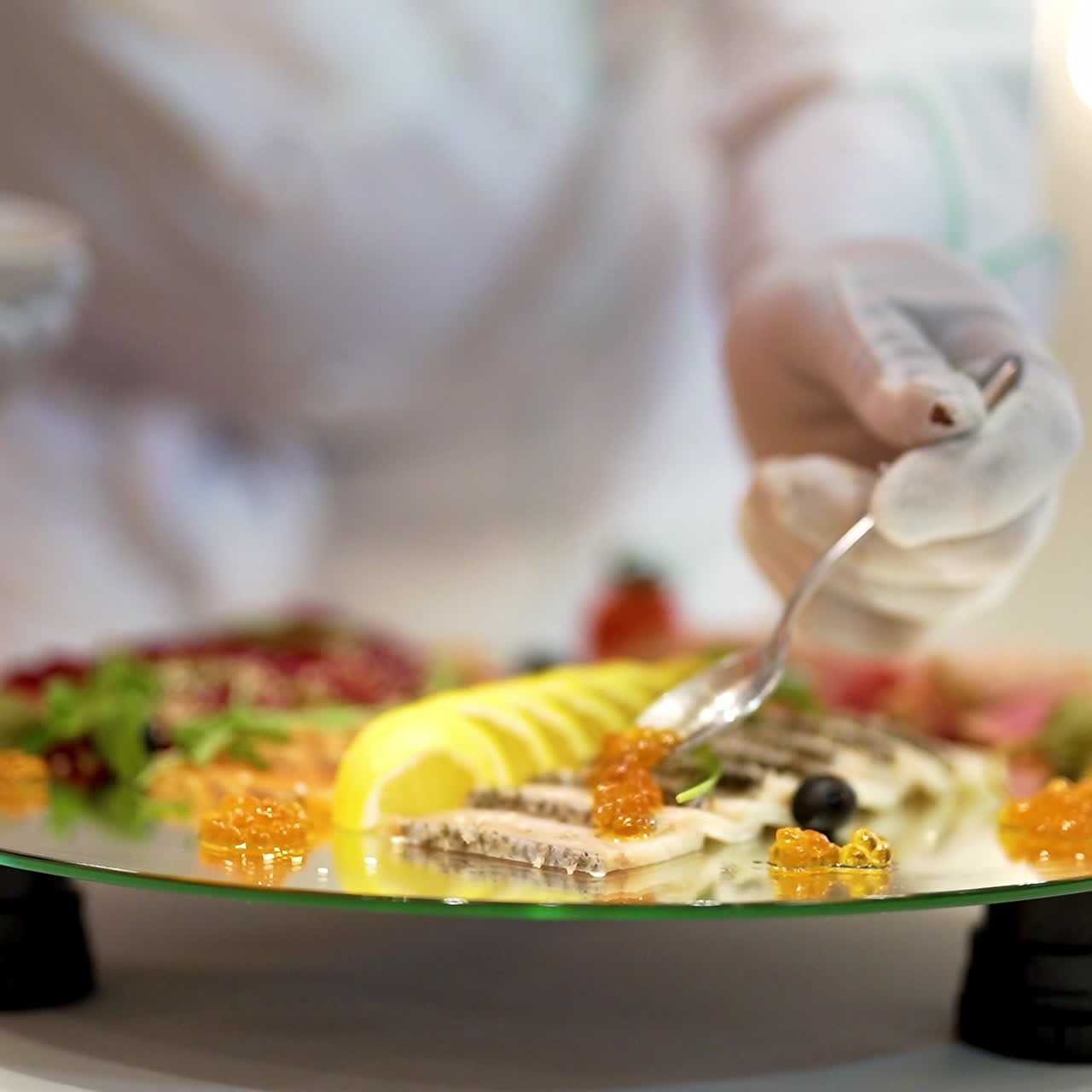 Professional cook is putting caviar by a spoon on the plate with some fruit and snacks of meat. Chief-cooker prepares food on a table in restaurant, delicious food is prepared for visitors