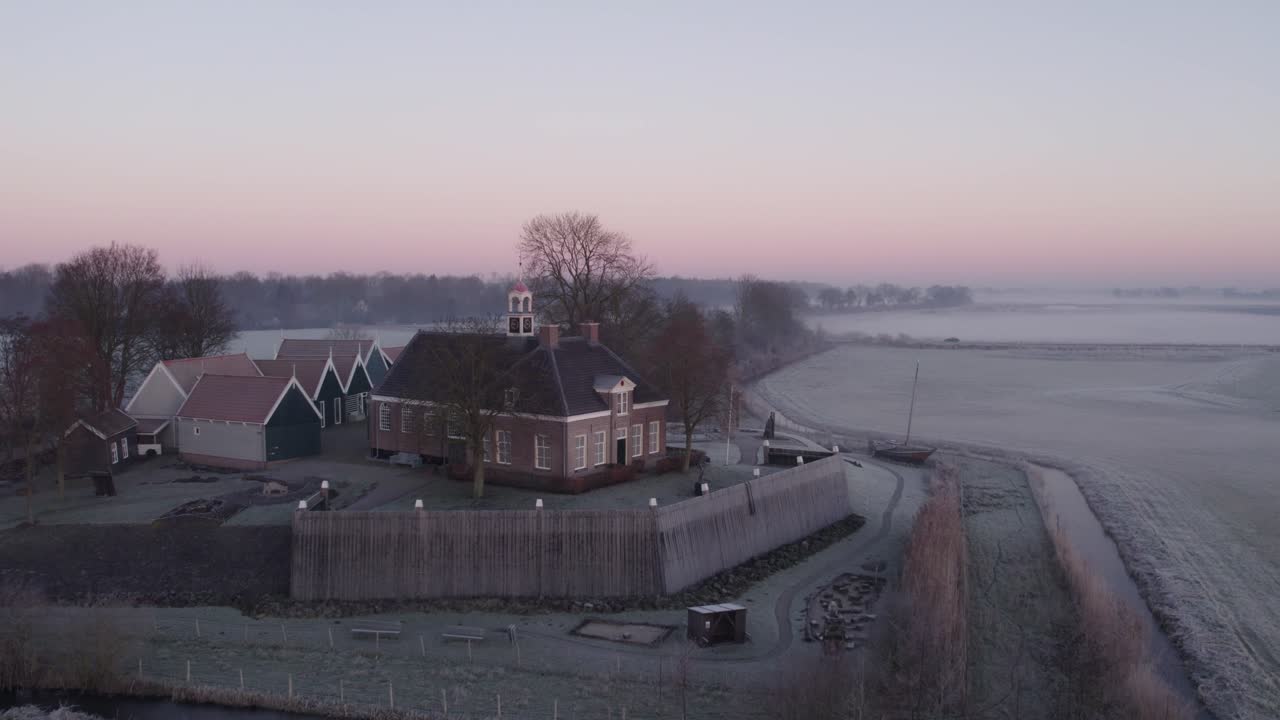 Landsby badet i varmt solopgangslys med kirke og træer, luftfoto, Schokland