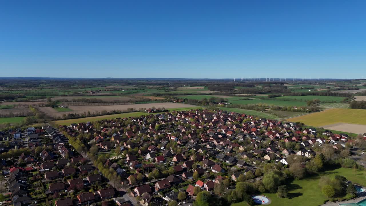 Aerial shot of quiet american neighborhood with single family houses and agricultural farm fields in Background. Sunny day with blue sky in spring season. Wind turbine in background.