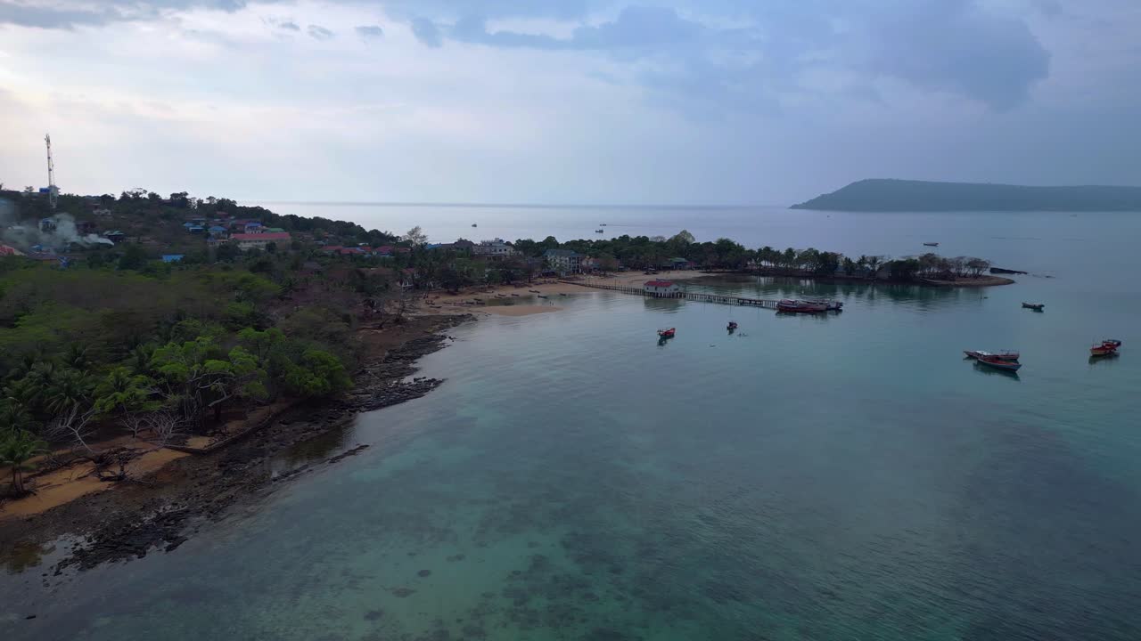 Koh Rong Sanloem island village in Cambodia, featuring turquoise water, pier, boats and tropical jungle. Lovely aerial view flight fly push forward drone