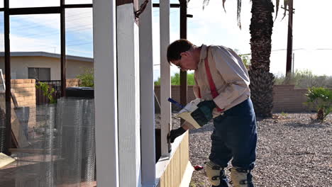 Dueño-De-Casa-Cepillando-Pintura-Blanca-En-El-Patio-De-Madera-Durante-La-Construcción-De-La-Casa