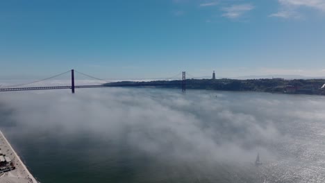 static drone shot of the river and ponte de 25 abril, portugal, in the fog.