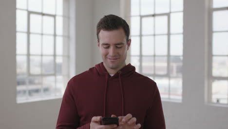 retrato de un apuesto joven caucásico enviando mensajes de texto navegando en línea utilizando la tecnología de redes sociales de teléfonos inteligentes en una nueva habitación de apartamento vacía