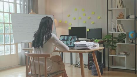 back view of asian woman having video call on laptop while working with documents at the office