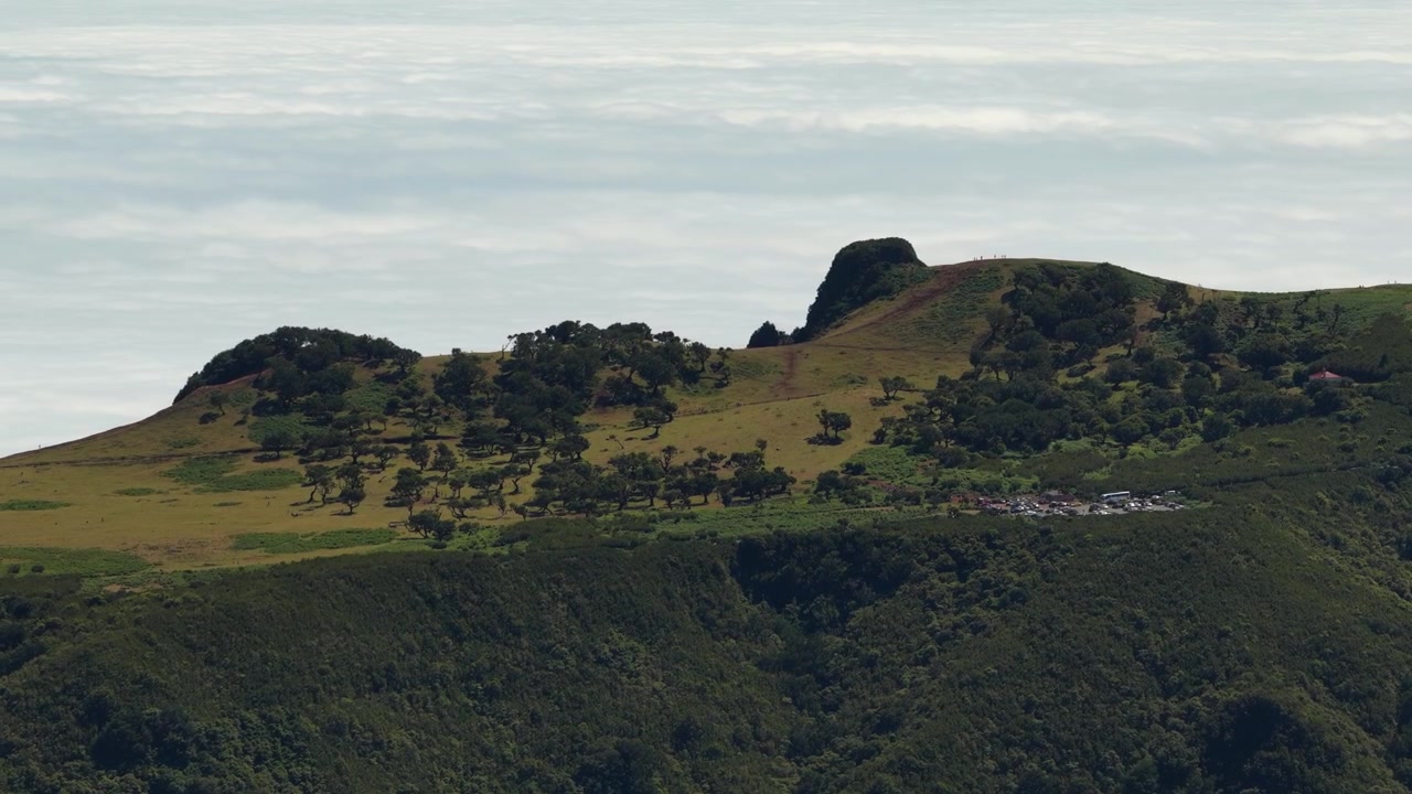 Vídeo aéreo de drone panorâmico captura as exuberantes árvores de laurissilva da floresta do Fanal, colinas verdes ondulantes e dramáticas cristas vulcânicas na ilha da Madeira, com nuvens melancólicas cobrindo o cénico sítio da UNESCO