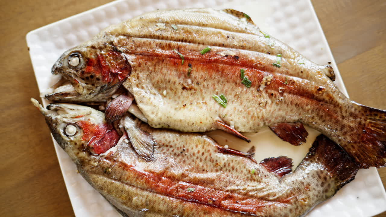 Two seasoned, grilled trouts on a white plate
