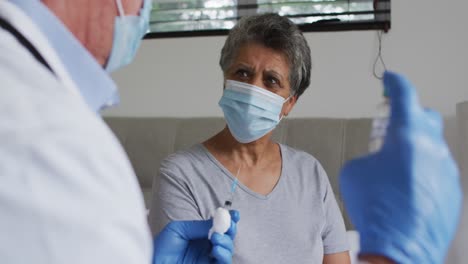 caucasian male doctor preparing vaccination for senior african american woman at home