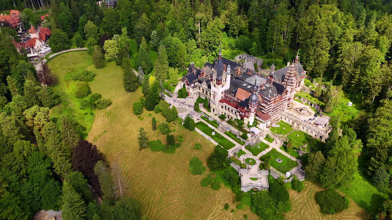 Beautiful territory of large Peles Castle, Prahova County, Romania surrounded by lush greenery. Lots of people stand at the entrance to the famous landmark