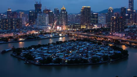 an aerial view showcases a small island in the river, covered with simple homes amidst a backdrop of towering skyscrapers.