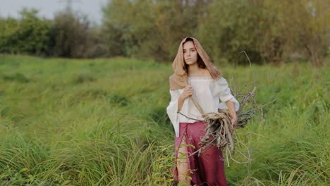 woman in medieval attire gathering wood in a field