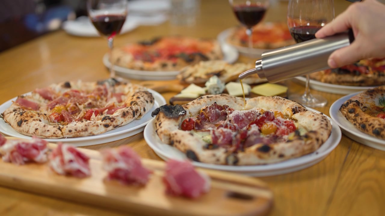 Primo piano di una mano che versa olio d'oliva su una pizza gourmet durante una cena in un ristorante italiano rustico.