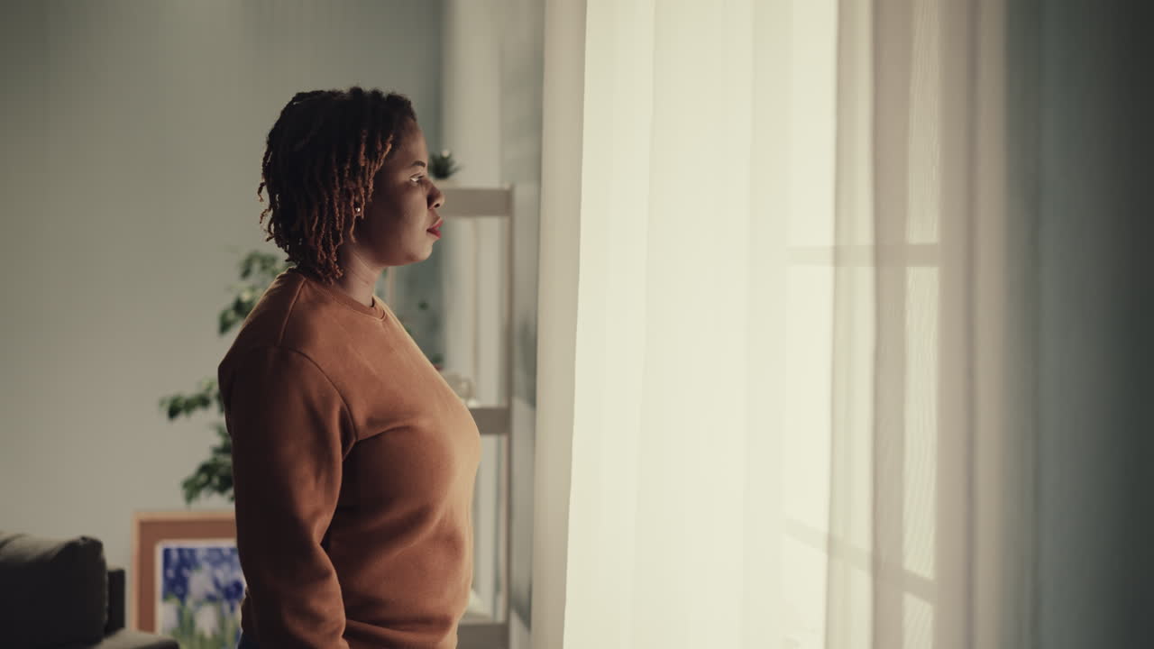 Thoughtful African American woman comes to bright window