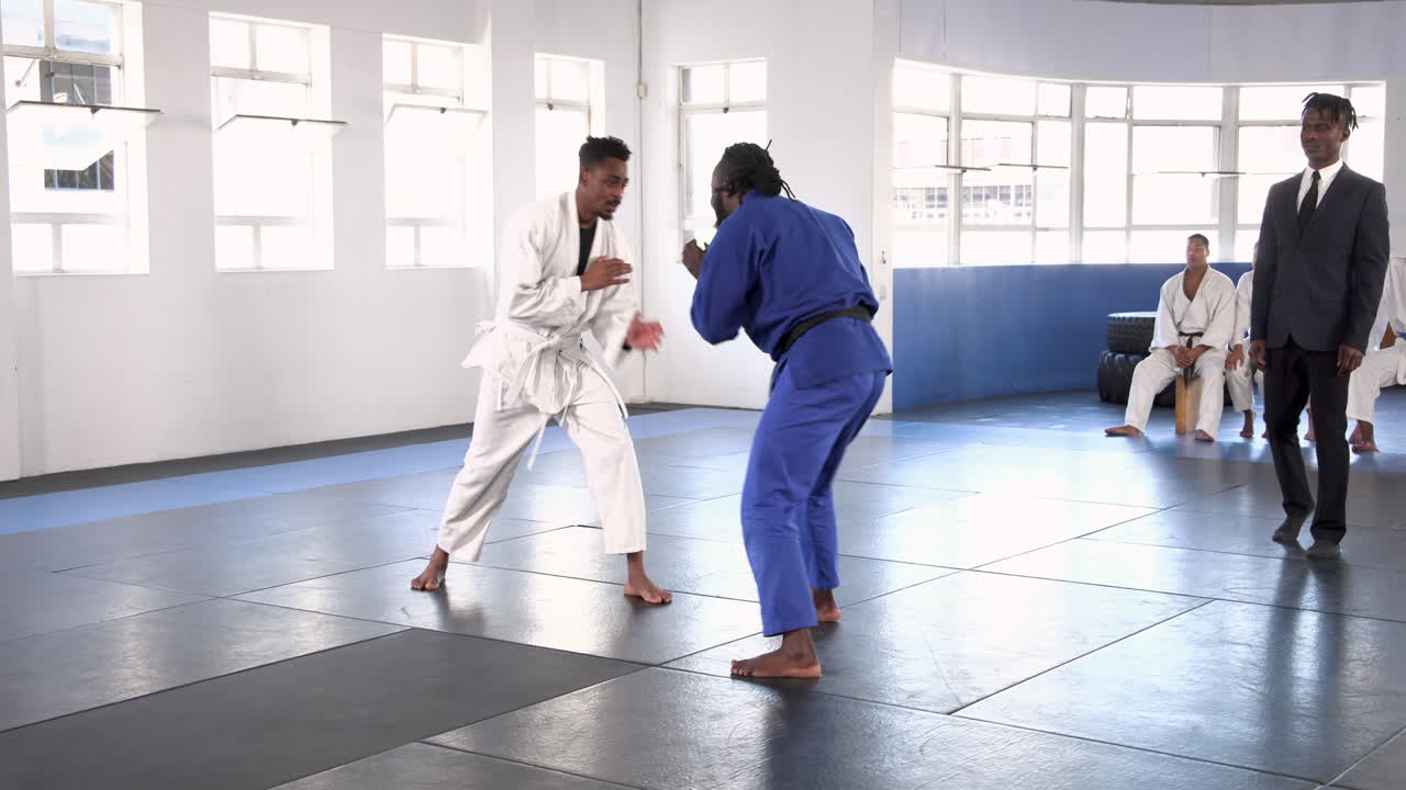 Practicing judo, athletes sparring on mat while instructor observes in dojo