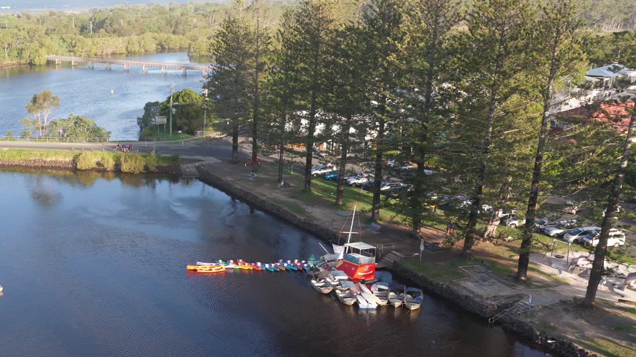 Drone footage captures boats docked along Brunswick River, surrounded by lush trees and calm waters under clear skies