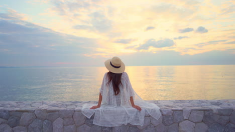 Back-view-of-a-woman-admiring-a-spectacular-sunset-with-cloudy-dramatic-sky-and-colourful-reflection-on-the-ocean