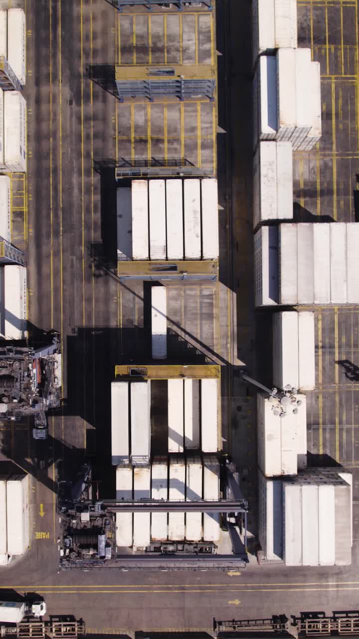 Overhead view of container handling area with cranes and neatly organized stacked units. Aerial, Vertical Video, Push forward