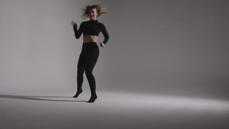 full length studio shot of young woman doing dance practise against grey background