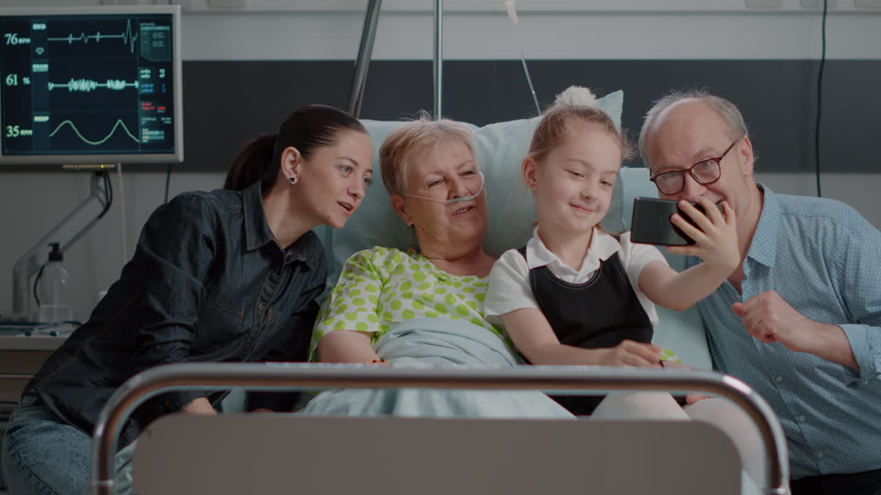 Family taking pictures with old patient in hospital ward