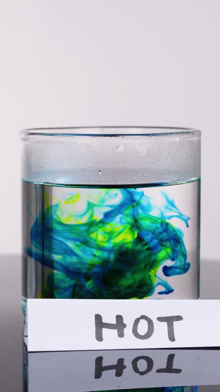 Il colorante colorato si disperde rapidamente in un bicchiere d'acqua calda, dimostrando la diffusione con una luminosa illuminazione da studio