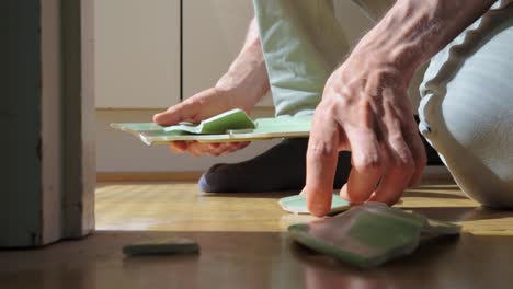 man picking up the pieces of broken plate from a wooden floor