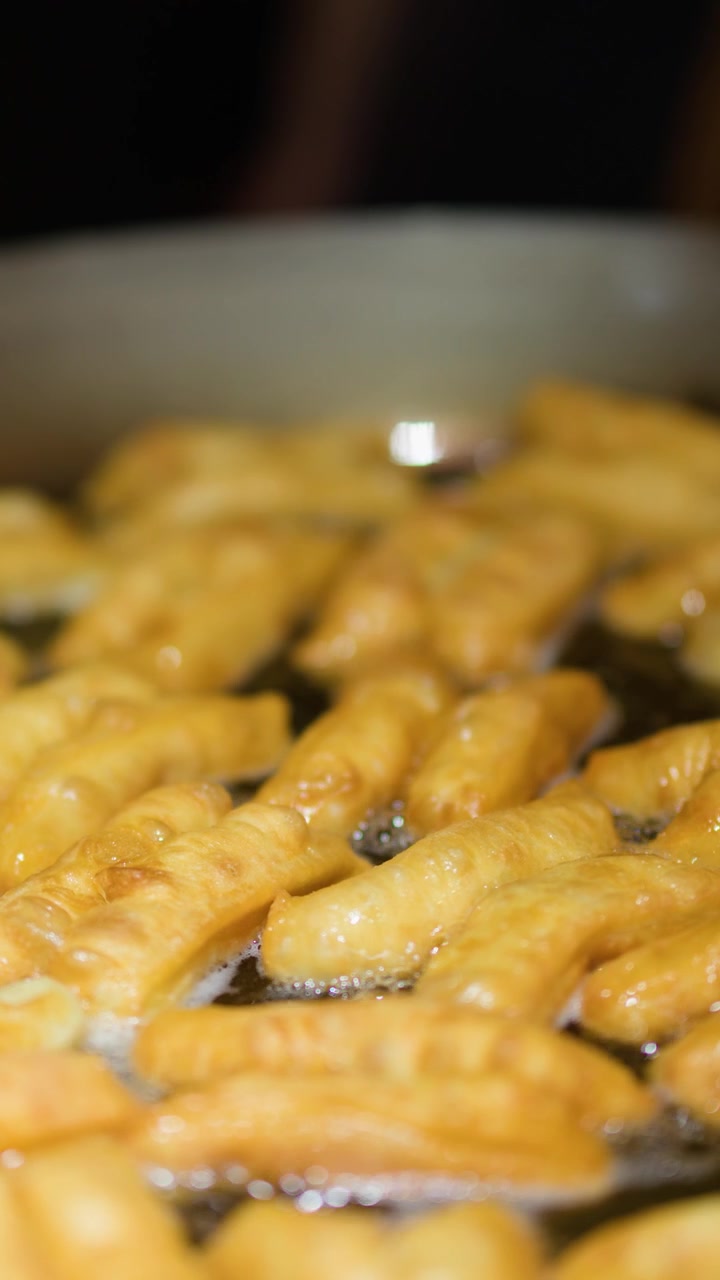 Friggere Youtiao (ciambelle cinesi) in olio bollente