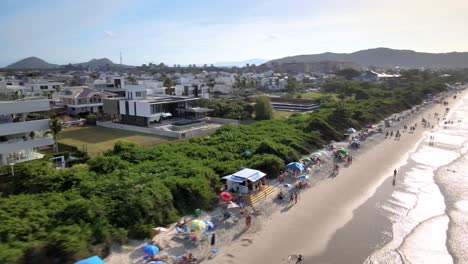 Escena-Aérea-De-Drones-De-Playa-Turística-Con-Muchas-Casas-De-Verano-Hoteles-Frente-Al-Mar-Malla-De-Playa-Urbana-Con-Mucha-Gente-Disfrutando-Del-Sol-La-Arena-Y-El-Mar-Florianópolis-Jurere-Internacional