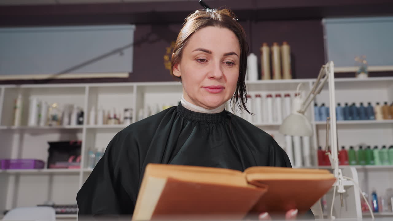 Primer plano de una mujer leyendo junto a una estantería en un salón de belleza; la vista en retrato muestra a una clienta concentrada hojeando las páginas, mientras que las estanterías llenas de botes de esmalte y productos forman el fondo, con iluminación cálida y profesional