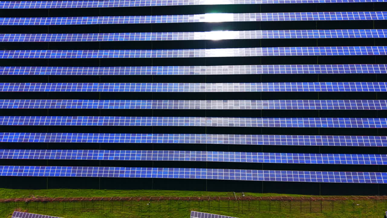 Prospettiva aerea dall'alto di una centrale solare fotovoltaica con pannelli blu e riflesso della luce solare. File di pannelli solari che riflettono la forte luce del sole.