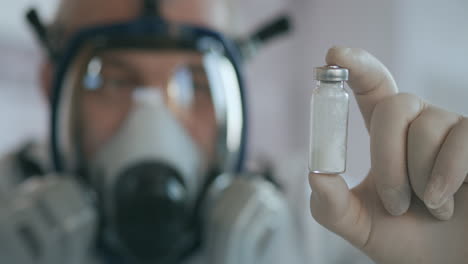 A-scientist-doctor-in-a-pharmaceutical-company-developing-a-drug-in-a-laboratory-in-a-glass-respirator-screen-holds-a-new-medicine-an-amulet-of-white-powder-with-a-vaccine-against-the-virus-and-looks.-High-quality-4k-footage