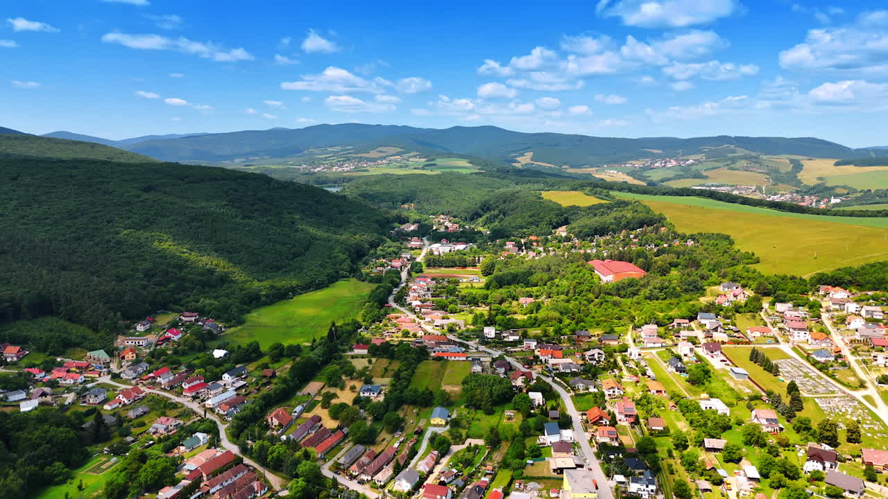 Luftaufnahme eines europäischen Dorfes. Blick auf ein malerisches Dorf, umgeben von grünen Hügeln und Feldern unter klarem blauem Himmel an einem sonnigen Tag