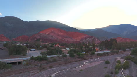 drone advancing over a dry riverbed and revealing the picturesque village of purmamarca with its famous "cerro de los 7 colores"