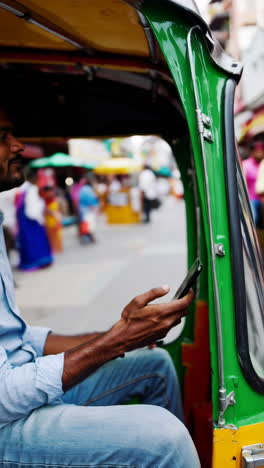 man using smartphone in an auto-rickshaw on a busy street