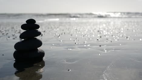 rock balancing on ocean beach, stones stacking by sea water waves. pyramid of pebbles on sandy shore