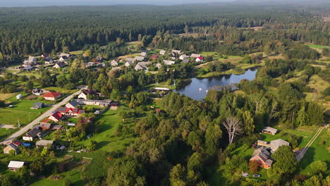scenic aerial of a lakeside village surrounded by forest and fields in pavilosta, latvia.