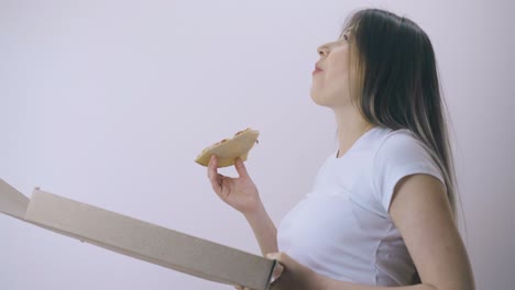 pregnant woman with tummy holds box of pizza at light wall