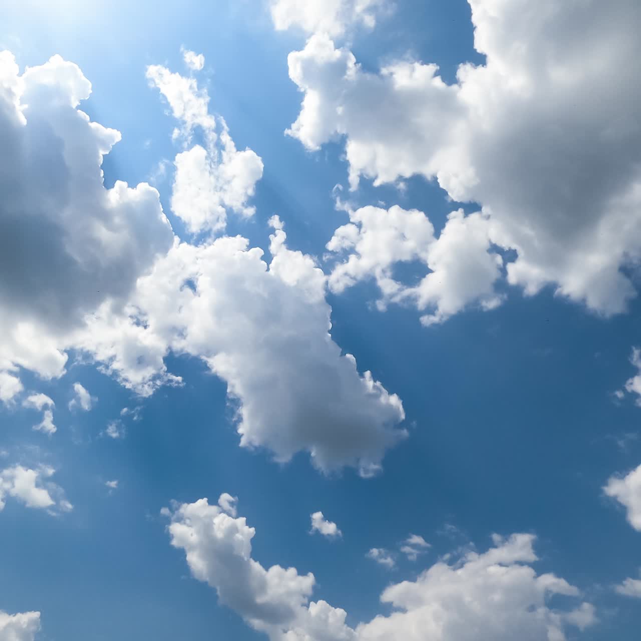 Lovely fluffy clouds in the rays of bright sky. Shape-changing cloudscape on beautiful sunny day from low angle view. Timelapse