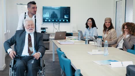 un colega empuja a un anciano empresario en silla de ruedas después de que una reunión de conferencia de negocios haya terminado