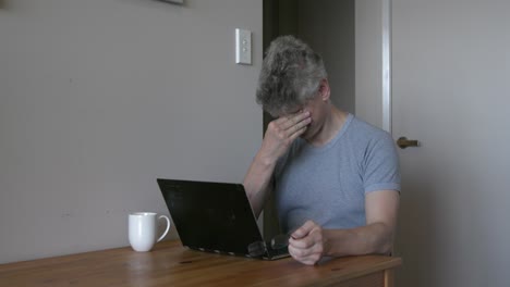 Mature-man-wearing-glasses-rubs-tired-eyes-overworked-typing-on-laptop