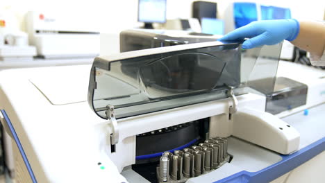 Medical laboratory assistant places a stand with a test tube into the machine. Female hand in gloves closes the lid in equipment to start the testing procedure.