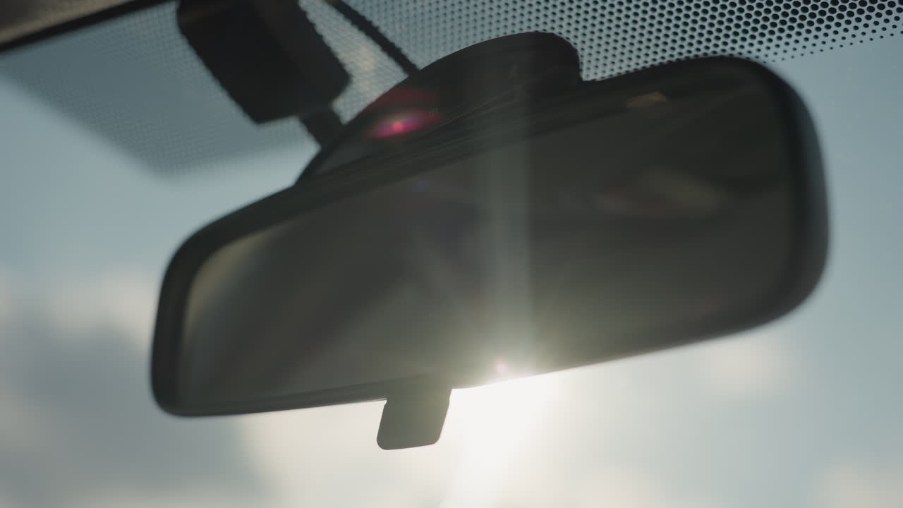 rearview mirror inside vehicle illuminated by intense sunlight with subtle flare effect casting warm glow on dark reflective surface creating cinematic mood under clear sky background