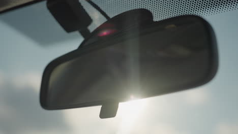 rearview mirror inside vehicle illuminated by intense sunlight with subtle flare effect casting warm glow on dark reflective surface creating cinematic mood under clear sky background