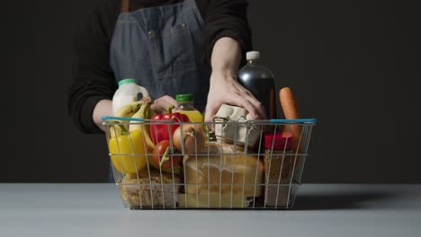 foto de estudio de un trabajador de la tienda revisando los alimentos básicos en la cesta de la compra de alambre del supermercado 3