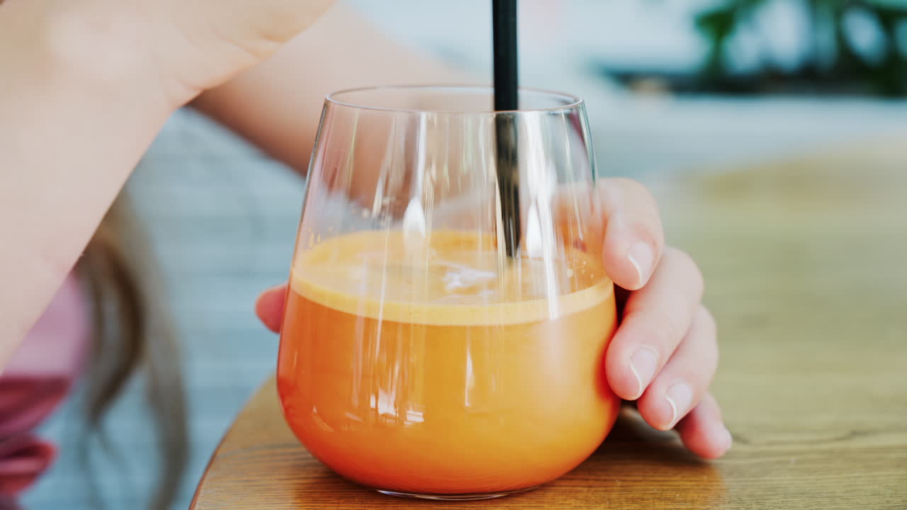 Close up of a woman mixing in a glass of orange juice with a black straw