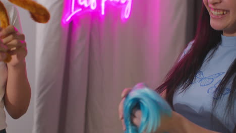 close up of two female friends choosing wigs and props outside photo booth with neon "let's party" sign outside