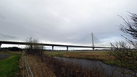 Speeding-time-lapse-traffic-passing-rural-countryside-suspension-bridge-over-dense-canal-wilderness