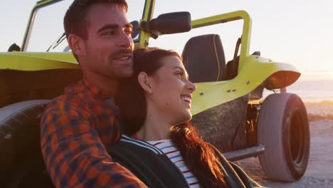 feliz pareja caucásica sentada al lado de la playa en un buggy junto al mar hablando abrazándose