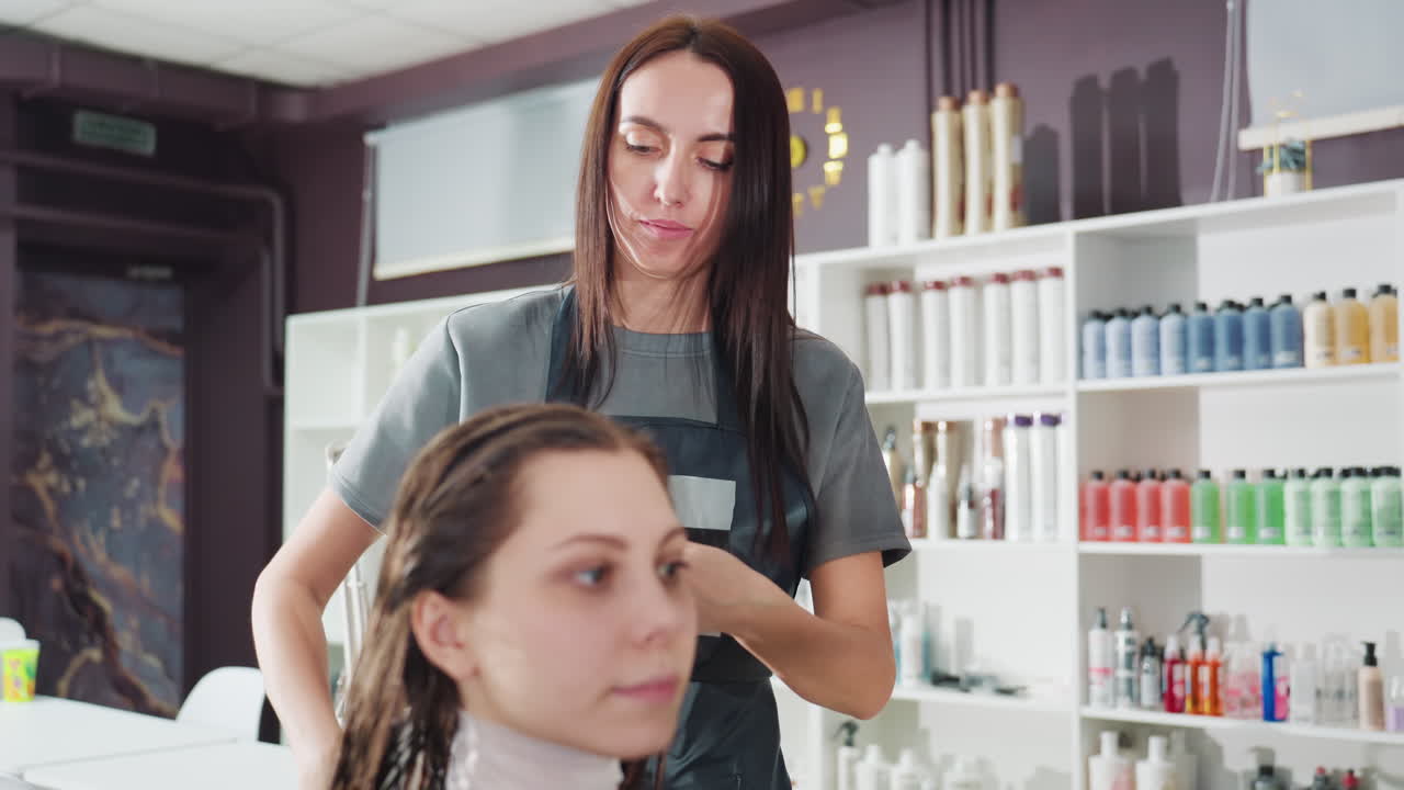 스타일리스트가 집중적으로 시술하며 뿌리부터 아래쪽으로 트리트먼트를 바르고, 전문 스타일리스트가 젖은 머리카락을 조심스럽게 관리하며, 현대적인 헤어 디자이너가 젖은 머리카락 뿌리부터 끝까지 능숙하게 코팅해요.