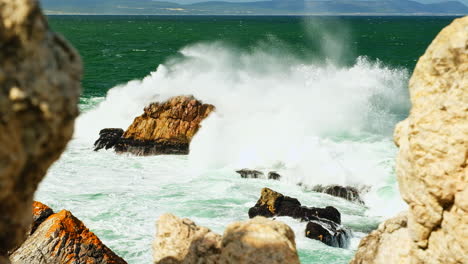 waves smash violently into rock in ocean, view framed from between rocks