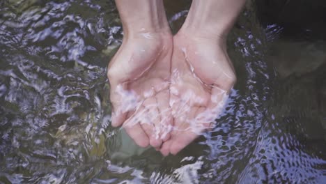 one hand lifts the stream water with the palm of the hand. slow motion.